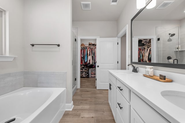 bathroom featuring wood finished floors, a shower stall, a bath, double vanity, and a walk in closet