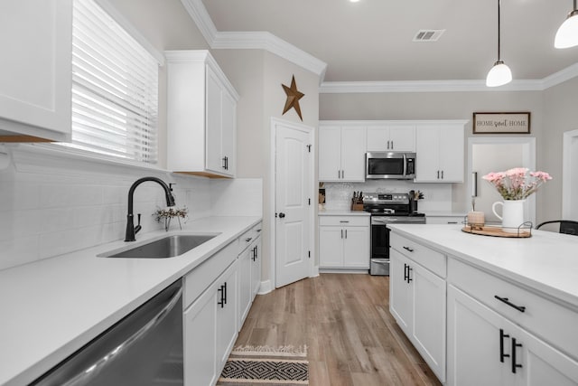 kitchen with appliances with stainless steel finishes, a sink, backsplash, white cabinetry, and light countertops