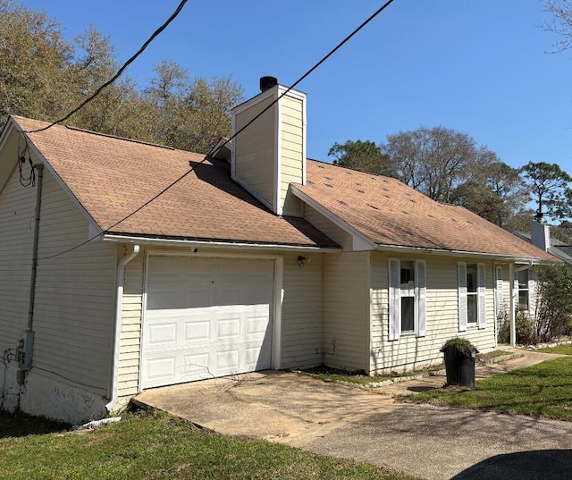 view of side of property with a chimney, an attached garage, and driveway