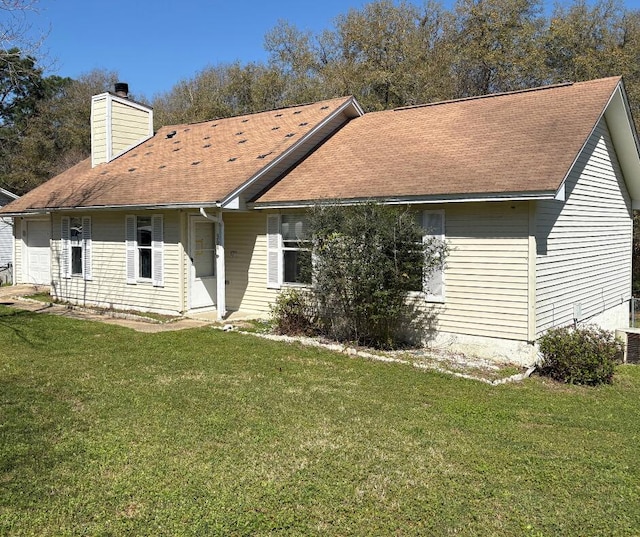 back of house featuring a chimney, a lawn, and a shingled roof