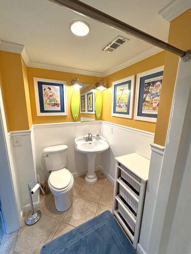 bathroom with wainscoting, crown molding, toilet, and tile patterned floors