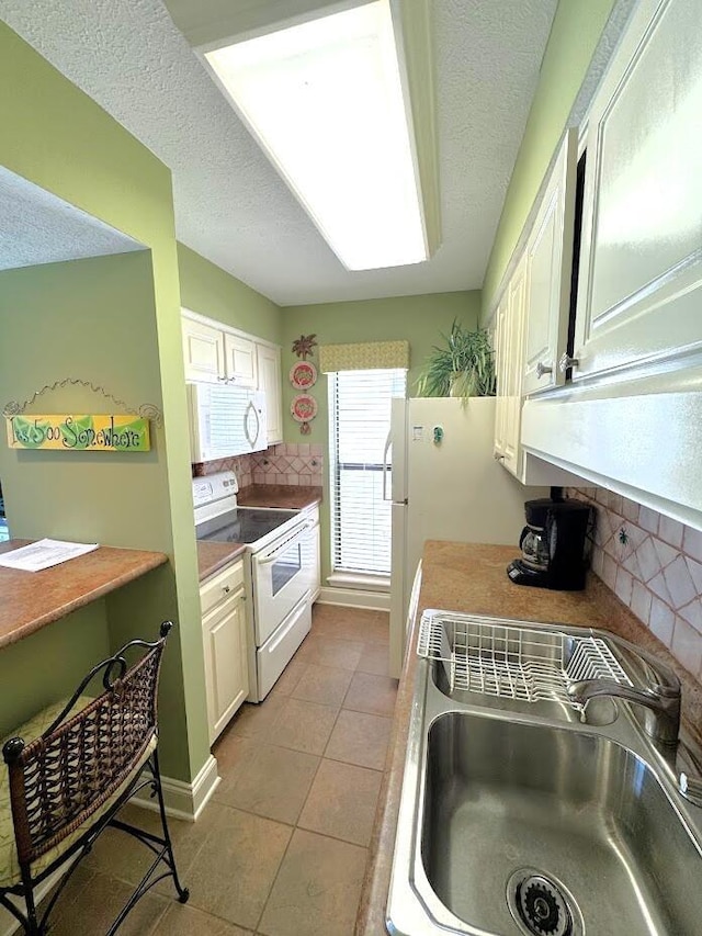 kitchen with white appliances, a sink, tasteful backsplash, light tile patterned floors, and a textured ceiling