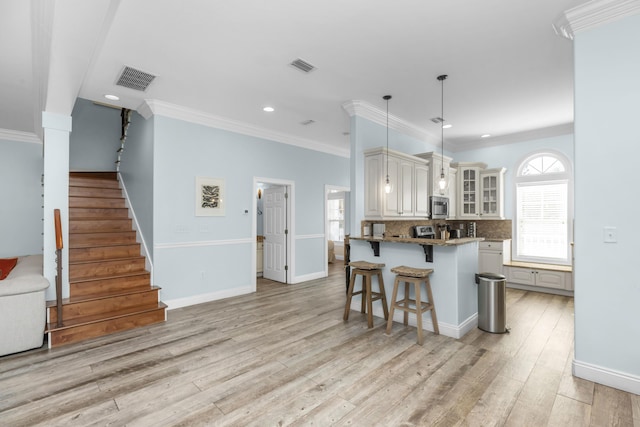kitchen with stainless steel microwave, a breakfast bar, glass insert cabinets, crown molding, and tasteful backsplash