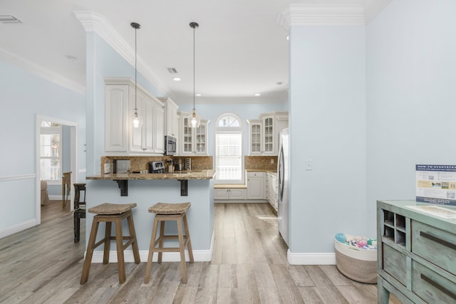 kitchen with stainless steel appliances, a peninsula, a kitchen breakfast bar, light stone counters, and glass insert cabinets