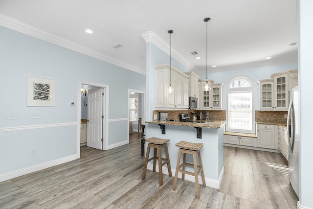 kitchen featuring appliances with stainless steel finishes, a kitchen bar, a peninsula, glass insert cabinets, and stone counters