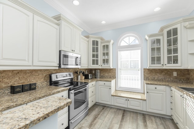 kitchen featuring stainless steel appliances, tasteful backsplash, glass insert cabinets, light wood-style flooring, and light stone countertops
