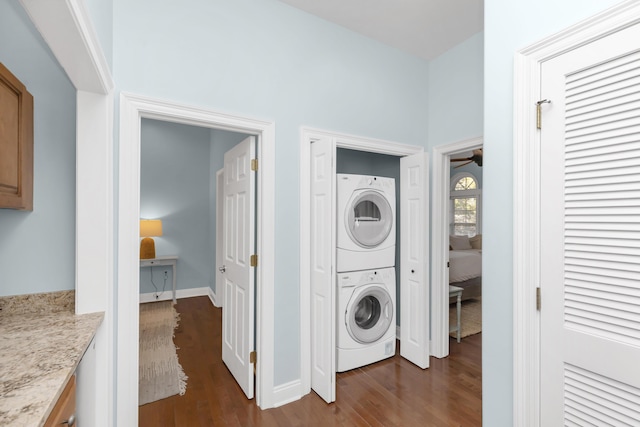 laundry area featuring stacked washing machine and dryer, dark wood-type flooring, baseboards, and a ceiling fan