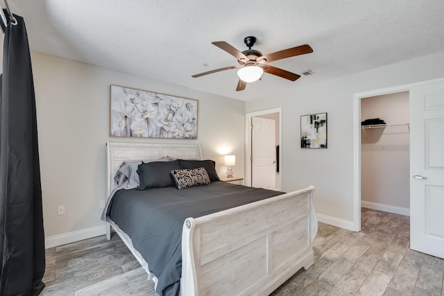 4274 Calinda Ln Unit 215, Niceville, FL 32578 - bedroom featuring light wood-style flooring, baseboards, a walk in closet, a textured ceiling, and ceiling fan
