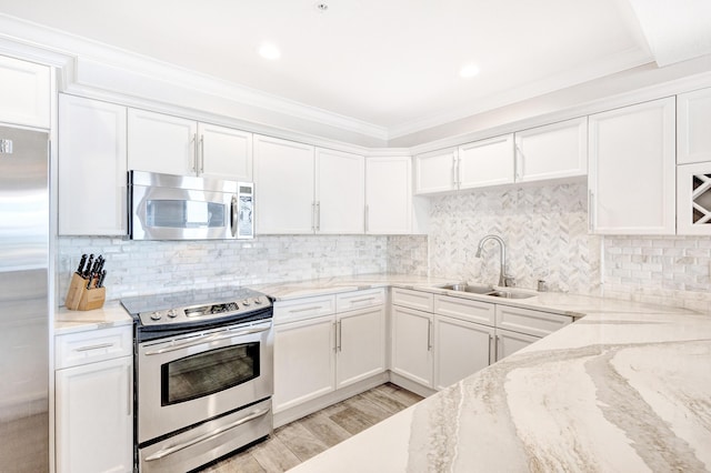 kitchen with stainless steel appliances, a sink, white cabinets, light stone counters, and light wood-type flooring