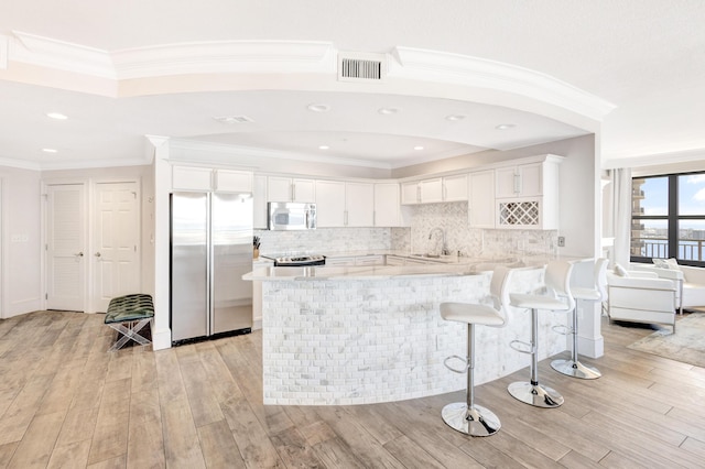 kitchen with stainless steel appliances, a sink, a peninsula, light wood-style floors, and ornamental molding