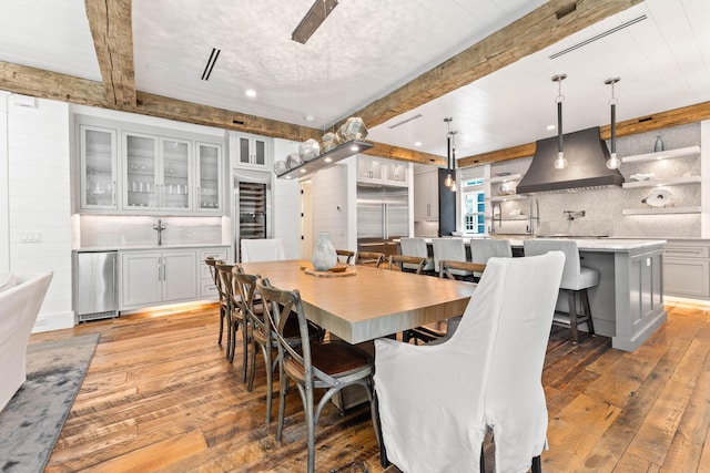 dining space with light wood-style floors, beamed ceiling, wine cooler, and recessed lighting