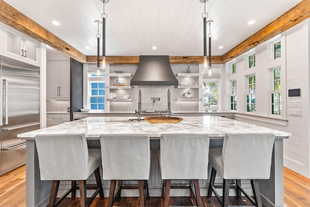 kitchen featuring built in refrigerator, custom exhaust hood, open shelves, recessed lighting, and wood finished floors