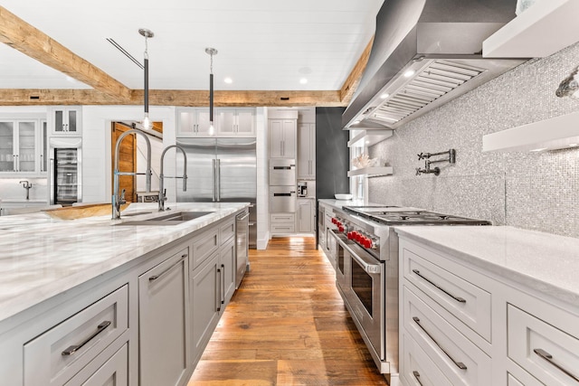 kitchen featuring high end appliances, wall chimney exhaust hood, beverage cooler, backsplash, and light wood-style floors