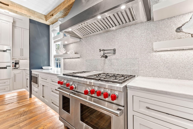 kitchen with range with two ovens, wall chimney exhaust hood, backsplash, light wood finished floors, and beam ceiling