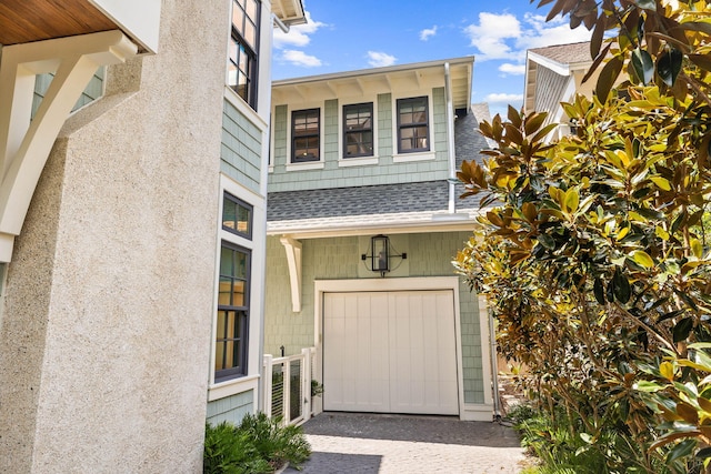 property entrance with a shingled roof, a garage, and driveway