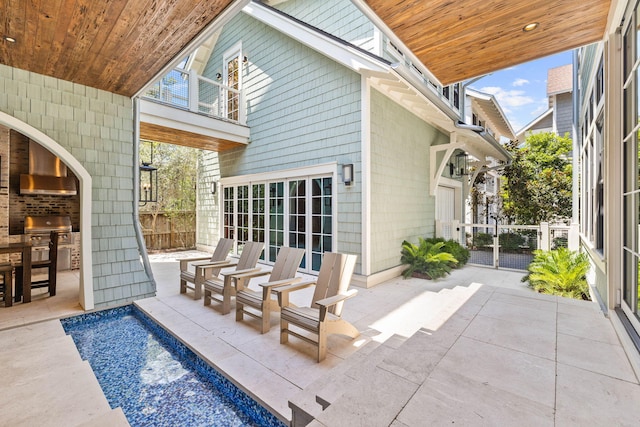 rear view of property with a balcony, a patio, an outdoor kitchen, and fence