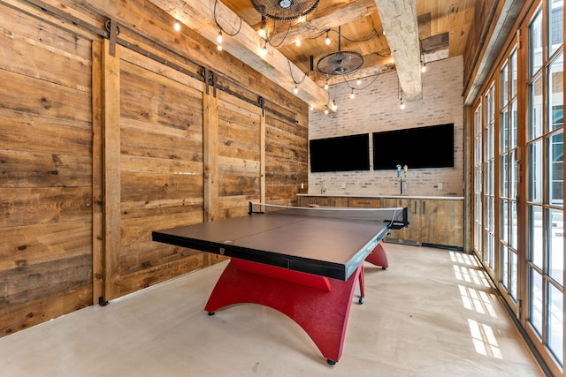 game room with a barn door, concrete flooring, beamed ceiling, wood ceiling, and wooden walls