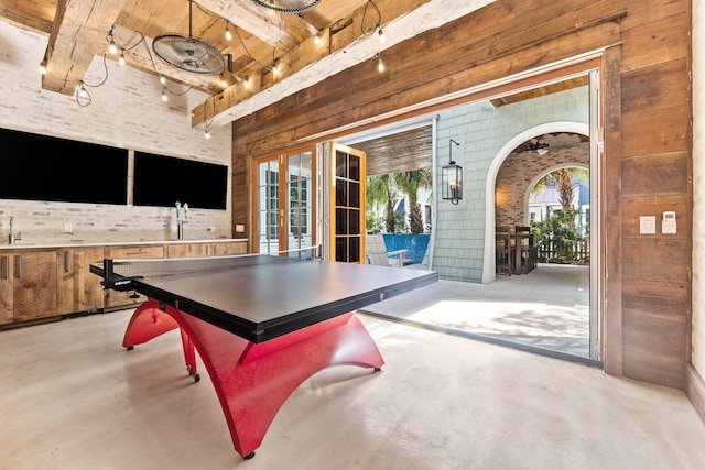playroom featuring french doors, finished concrete flooring, wooden walls, arched walkways, and beam ceiling