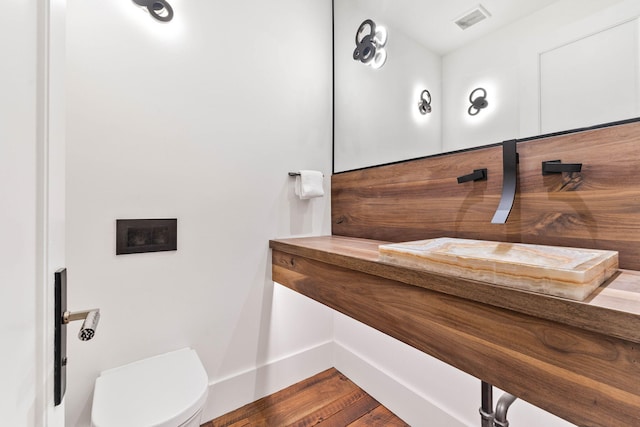 half bathroom with toilet and wood finished floors