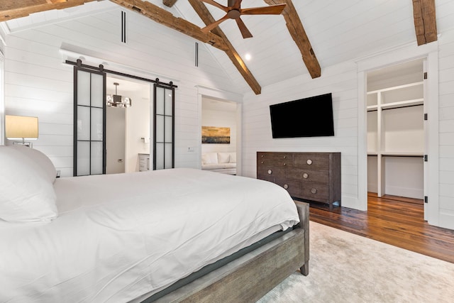 bedroom with a barn door, wood finished floors, wooden walls, and ceiling fan