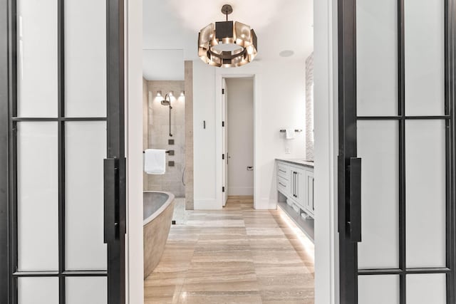 full bathroom with a chandelier, tiled shower, a freestanding bath, baseboards, and vanity