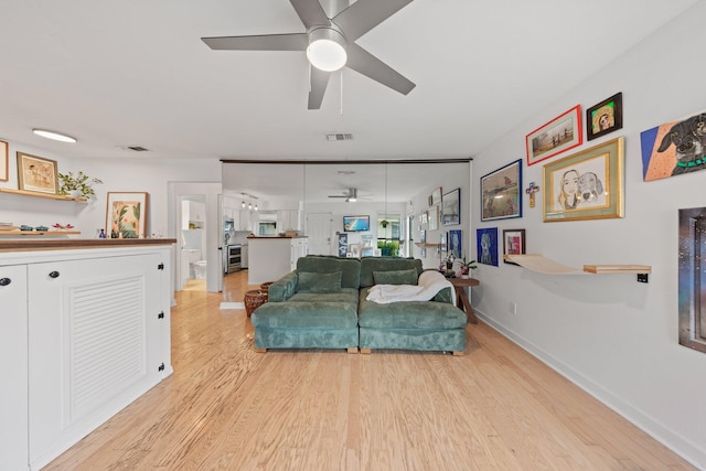 living area featuring a ceiling fan, light wood finished floors, and baseboards
