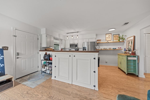 kitchen featuring appliances with stainless steel finishes, light wood finished floors, a peninsula, white cabinetry, and open shelves