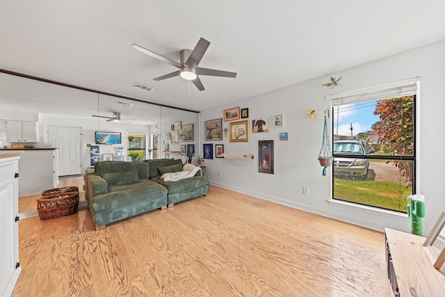 living area with a ceiling fan, light wood-style flooring, plenty of natural light, and baseboards