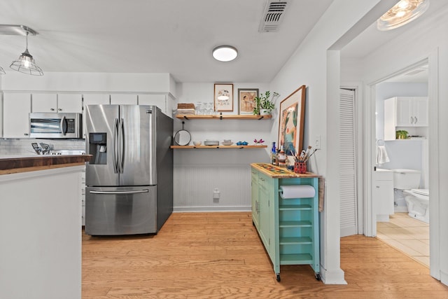 kitchen with stainless steel appliances, light wood finished floors, white cabinets, decorative backsplash, and a wainscoted wall