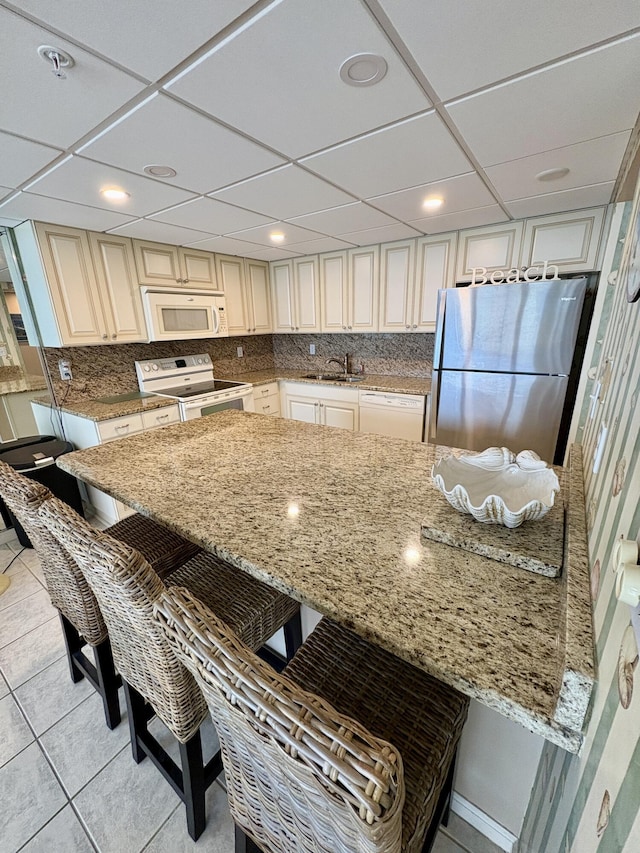 11347 Front Beach Rd # 601, Panama City Beach, FL 32407 - kitchen featuring white appliances, a sink, a kitchen bar, light stone counters, and backsplash