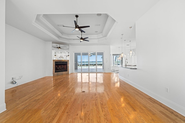 411 Calhoun Ave, Destin, FL 32541 - unfurnished living room featuring a raised ceiling, a ceiling fan, crown molding, light wood-style flooring, and a tile fireplace