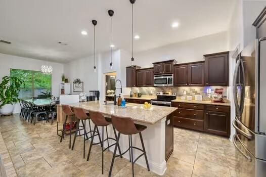 5930 Wind Trace Rd, Crestview, FL 32536 - kitchen with stainless steel appliances, tasteful backsplash, a kitchen breakfast bar, an island with sink, and dark brown cabinets
