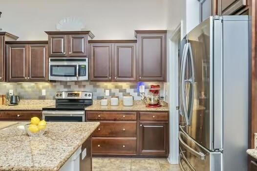 5930 Wind Trace Rd, Crestview, FL 32536 - kitchen featuring stainless steel appliances, light stone countertops, tasteful backsplash, dark brown cabinets, and light tile patterned floors