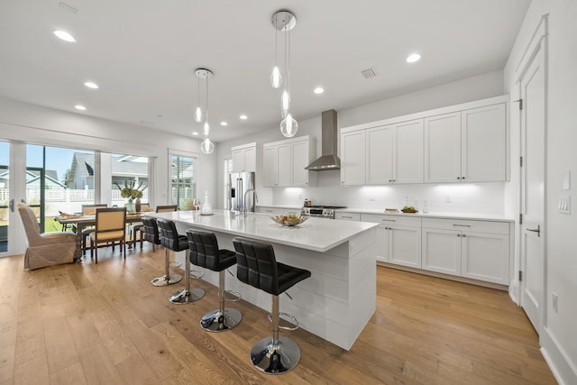 kitchen featuring wall chimney exhaust hood, light wood finished floors, a breakfast bar, light countertops, and a center island with sink