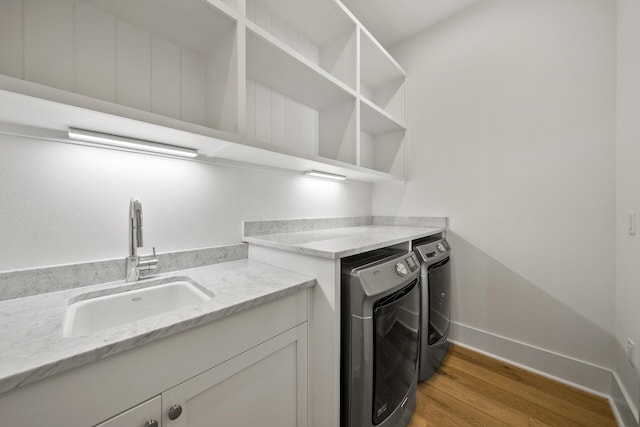 laundry area featuring washing machine and clothes dryer, a sink, wood finished floors, and baseboards