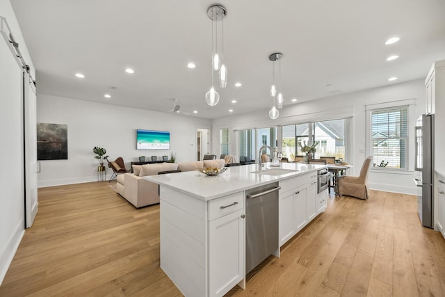 kitchen with a sink, stainless steel appliances, open floor plan, light wood finished floors, and recessed lighting