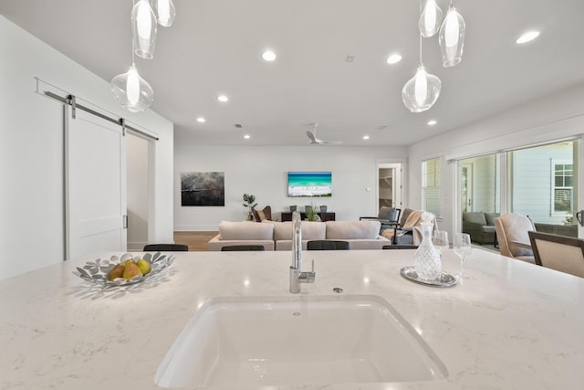 kitchen featuring open floor plan, a barn door, recessed lighting, light stone countertops, and pendant lighting