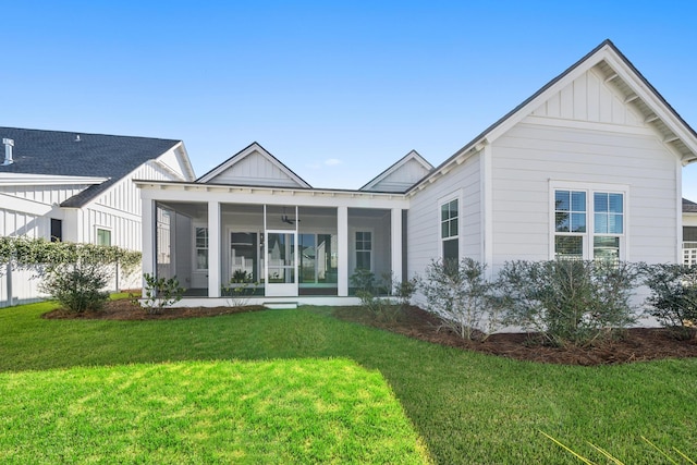 rear view of property featuring board and batten siding, a sunroom, and a yard
