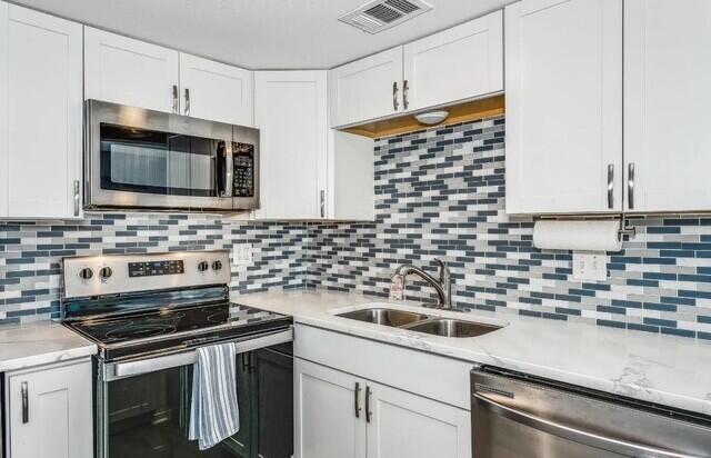 308 Miracle Strip Pkwy Unit 1C, Fort Walton Beach, FL 32548 - kitchen with stainless steel appliances, a sink, white cabinetry, and backsplash