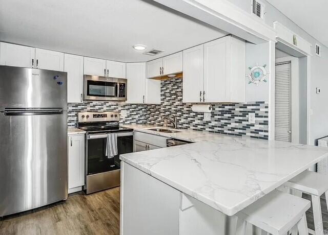 308 Miracle Strip Pkwy Unit 1C, Fort Walton Beach, FL 32548 - kitchen featuring stainless steel appliances, a peninsula, a sink, light stone countertops, and white cabinetry