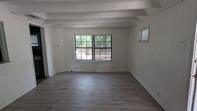 spare room with beam ceiling, wood finished floors, and wooden walls
