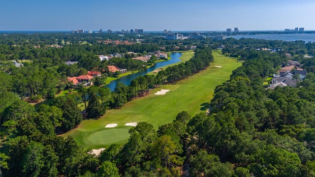 aerial overview of property's location featuring a golf course, a nearby body of water, nearby urban area, and a tree filled landscape