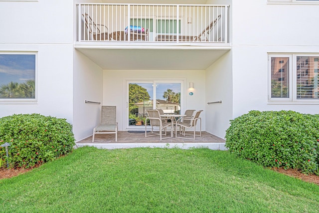 property entrance featuring stucco siding, a balcony, a patio, and a lawn