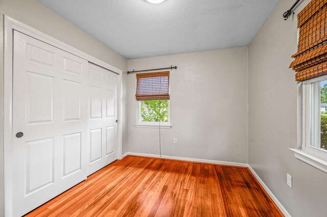 3 NE Windsor Ln, Fort Walton Beach, FL 32547 - unfurnished bedroom with light wood-style floors, multiple windows, baseboards, a textured ceiling, and a closet