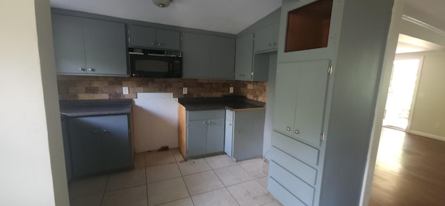 kitchen featuring black microwave, decorative backsplash, vaulted ceiling, gray cabinetry, and light tile patterned floors