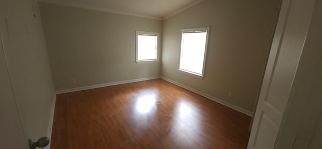 spare room featuring crown molding, wood finished floors, vaulted ceiling, and baseboards
