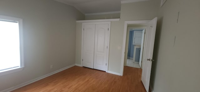 unfurnished bedroom featuring a closet, light wood-type flooring, baseboards, and ornamental molding
