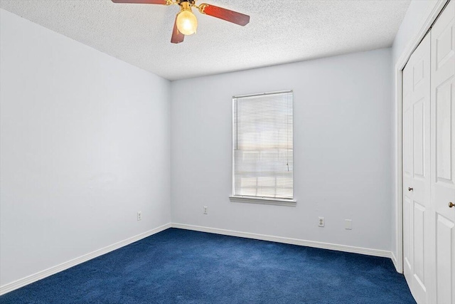 unfurnished bedroom featuring a closet, dark colored carpet, a textured ceiling, ceiling fan, and baseboards