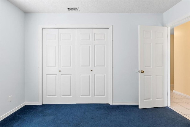 unfurnished bedroom with a closet, dark carpet, dark tile patterned flooring, baseboards, and a textured ceiling