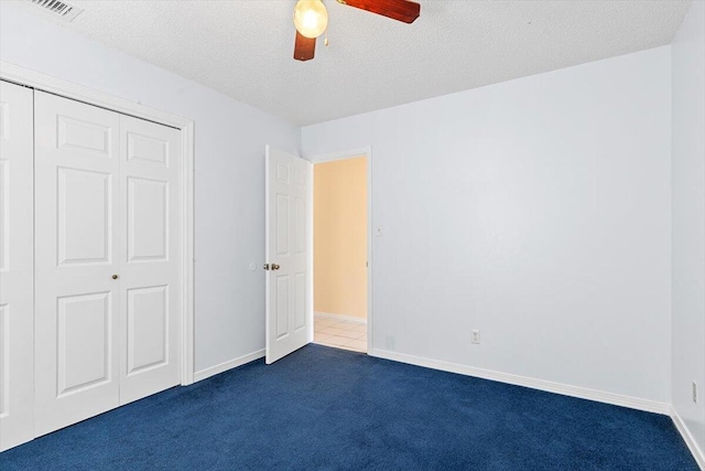 unfurnished bedroom featuring dark carpet, a closet, a ceiling fan, a textured ceiling, and baseboards
